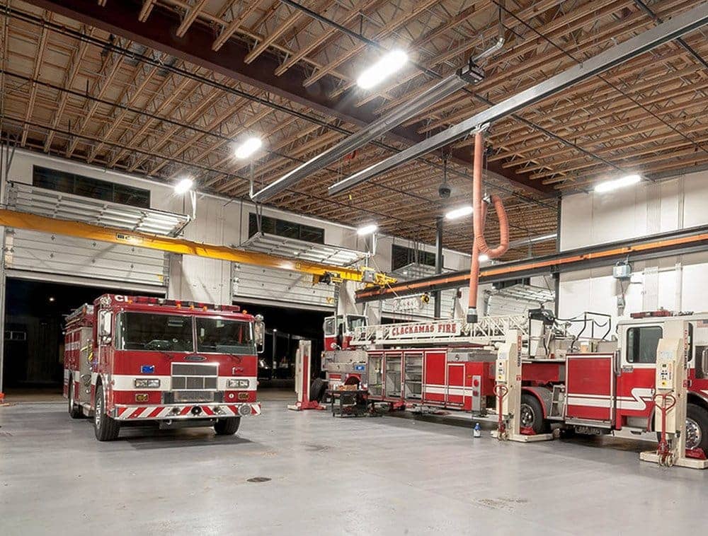 A fire station at night features open web trusses over its large trucks