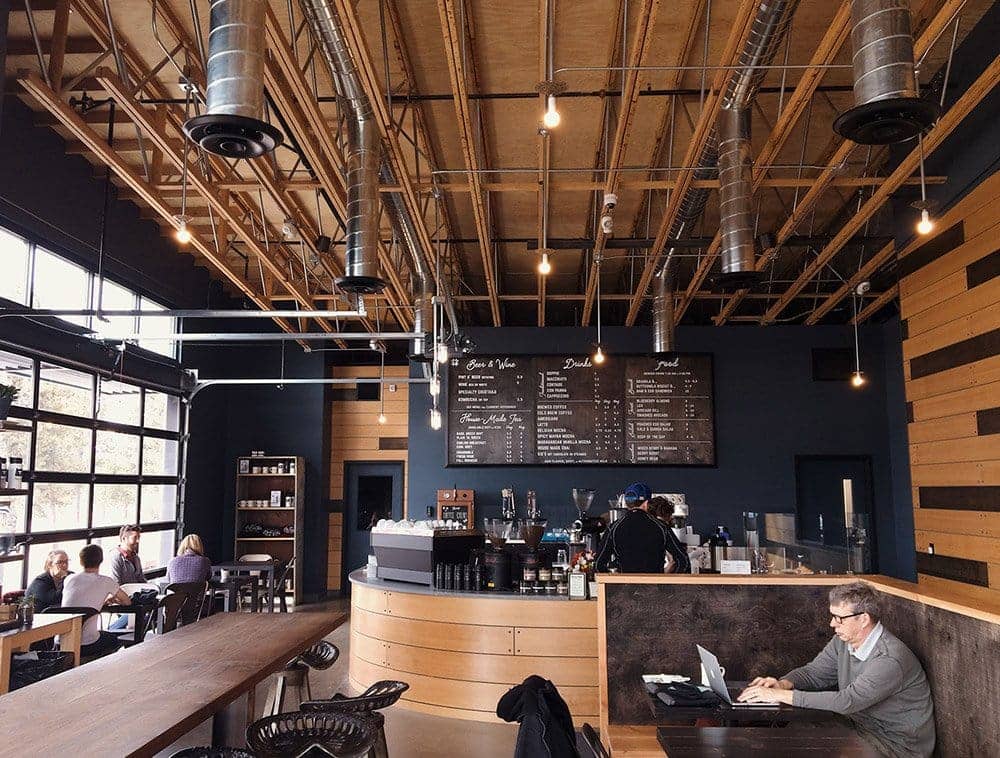 A cafe with patrons working and interacting, above are open web roof trusses